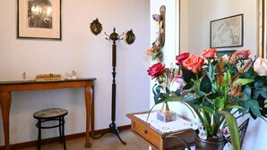 Una habitación con un escritorio de madera, una silla, un espejo, un florero con flores e iluminación en la pared.