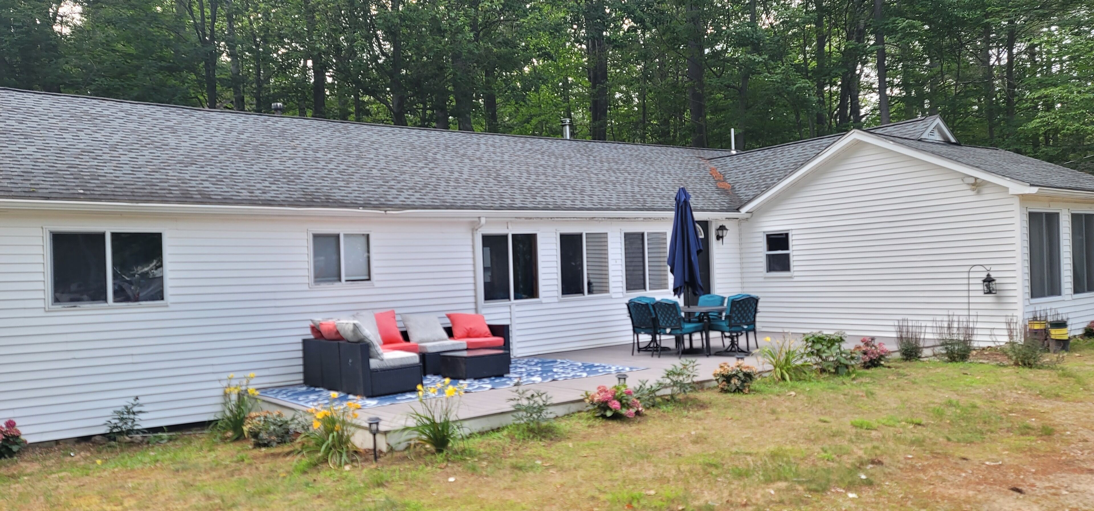 A white single-story house with a patio area featuring a black sofa set, a table with chairs, and a blue umbrella.