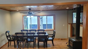Un comedor con una mesa y sillas de madera, un ventilador de techo y un ventanal con vistas al exterior.