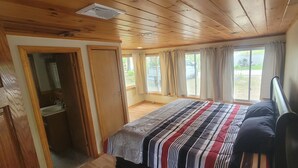 Un dormitorio de cabaña de madera con una cama, una mesita de noche y una ventana con cortinas.