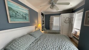 Ein Schlafzimmer mit einem großen Bett, einem Deckenventilator, einem Bild an der Wand und einem Fenster mit Jalousien.