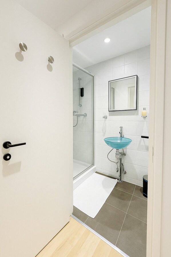 Une salle de bain moderne avec une douche à parois de verre, un lavabo en verre bleu et un sol carrelé de couleur blanche.
