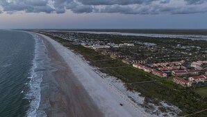 Luchtbeeld van een kustgebied met een strand, woongebouwen en een weg.