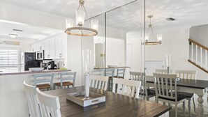 Een moderne keuken met witte kasten, een donker houten eettafel en hanglampen.