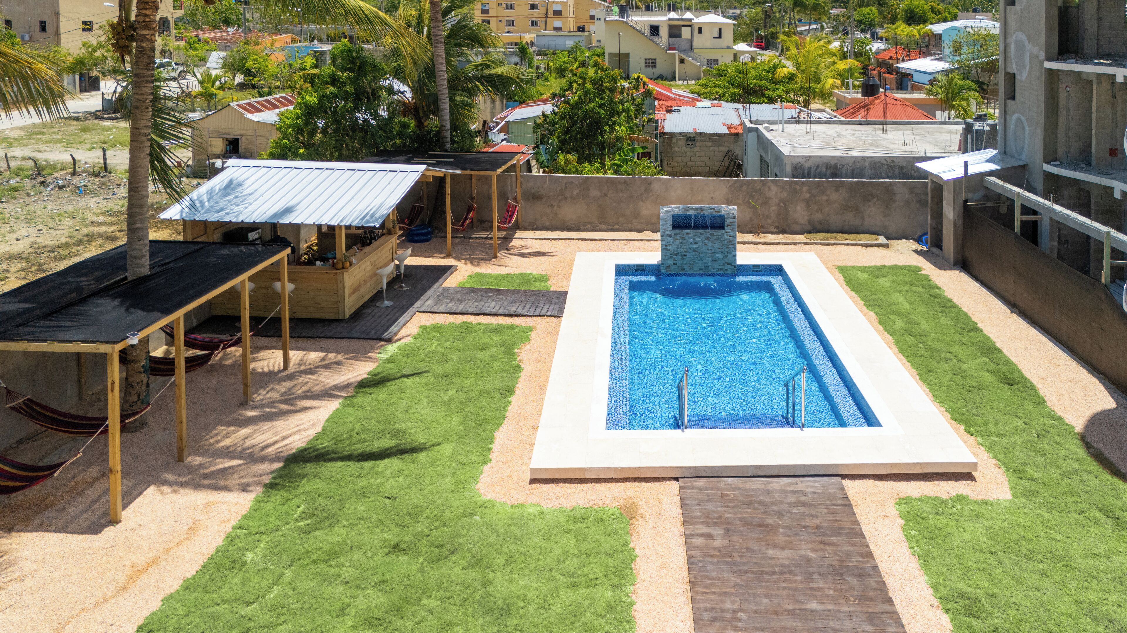 Ein Poolbereich auf dem Dach mit einem rechteckigen Pool, umgeben von grünem Kunstrasen, einer Holzterrasse und einer kleinen, überdachten Holzkonstruktion.