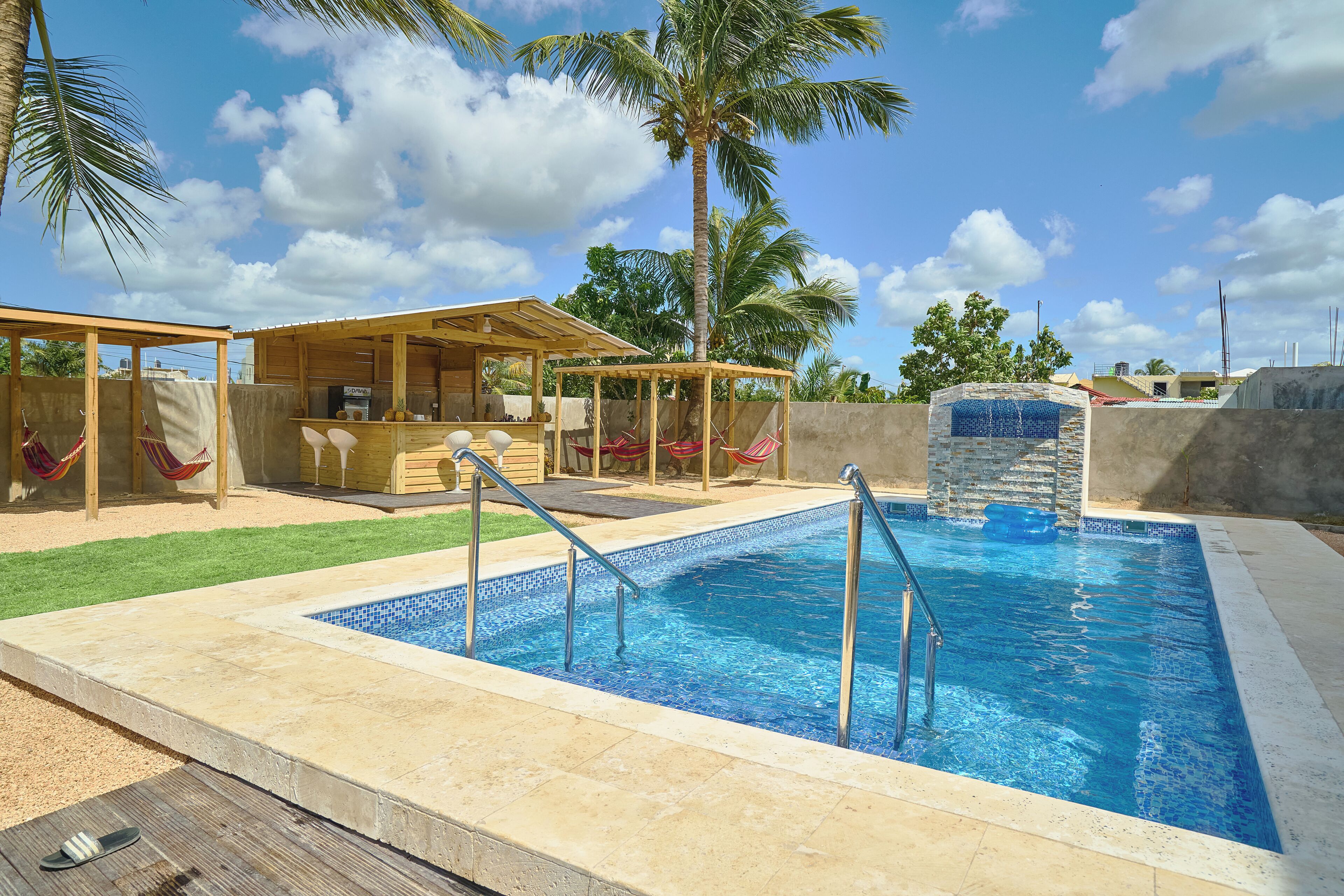 Une piscine avec une terrasse en bois, un espace salon couvert et des palmiers en arrière-plan.