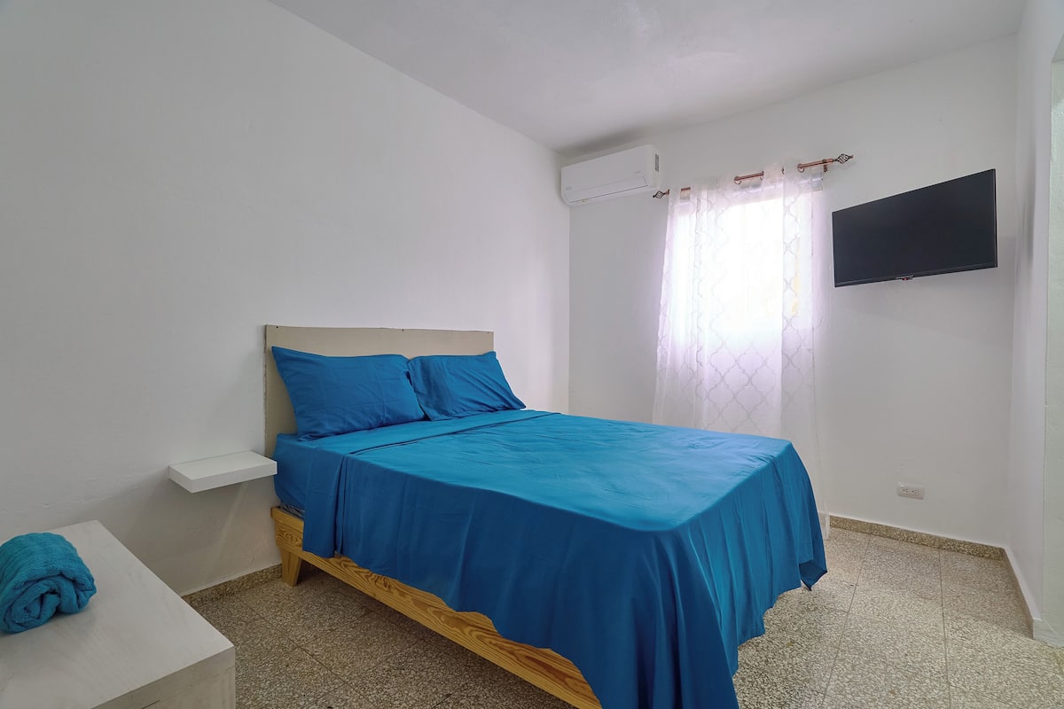 A bedroom with a bed, a TV, and an air conditioning unit.