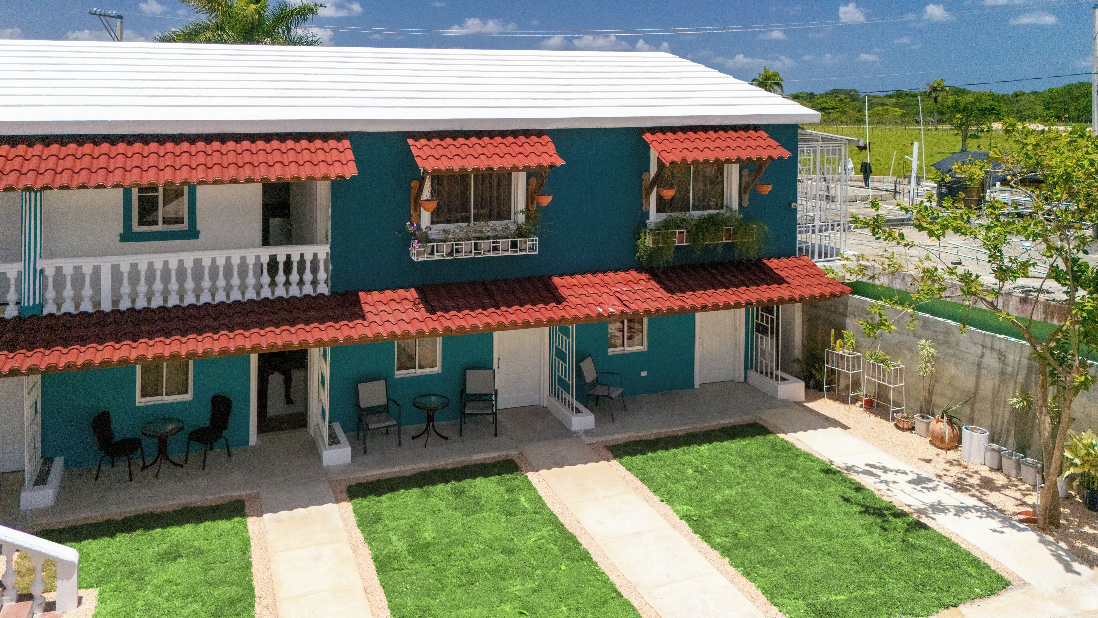 A two-story building with a red-tiled roof, a balcony with hanging plants, and a small patio area with outdoor seating.