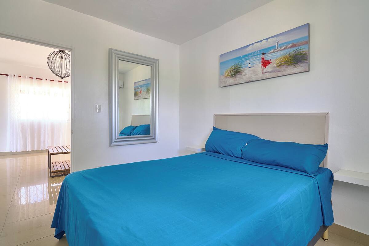 A bedroom with a bed, a painting, a mirror, and a bench.