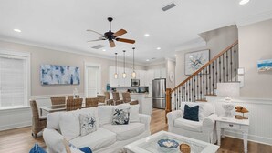 A spacious living room with a white sofa, a glass coffee table, and a dining area with wicker chairs.