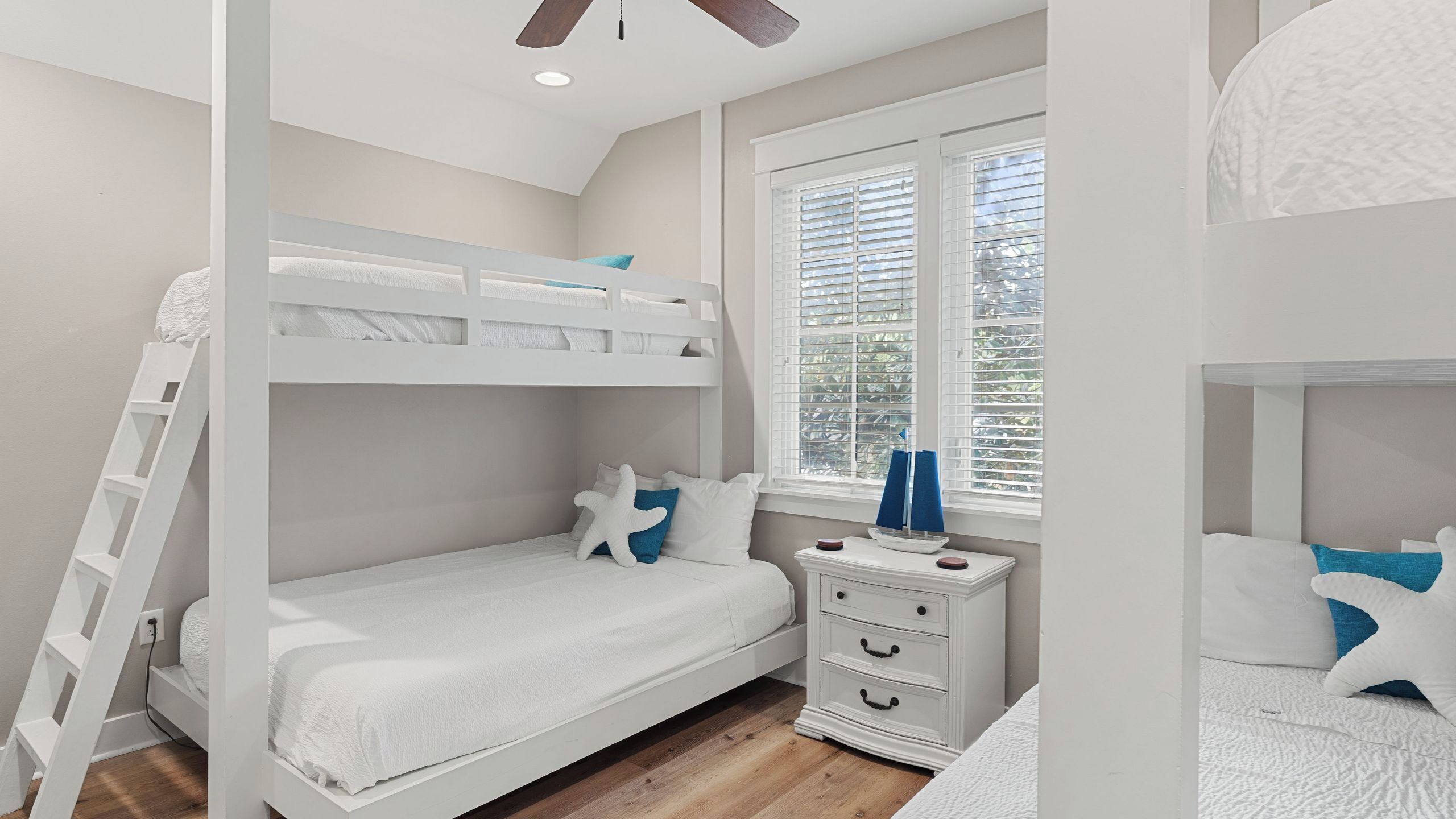 Une chambre avec un lit superposé, une fenêtre, une table de chevet et une commode.