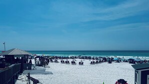 A beach with sun loungers and umbrellas, a wooden structure, and a clear view of the ocean.