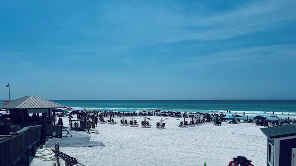 A beach with sun loungers and umbrellas, a wooden structure, and a clear view of the ocean.