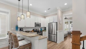 A modern kitchen with white cabinetry, stainless steel appliances, and a central island with bar stools.