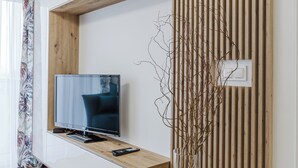 Una sala de estar moderna con un televisor de pantalla plana sobre un estante de madera, un control remoto y una rama decorativa en un florero de vidrio.