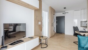 Una sala de estar moderna con un televisor de pantalla plana, vigas de madera, una mesita y un sillón verde azulado.