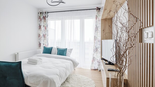 Un dormitorio moderno con una cama, un escritorio con una computadora y un televisor.