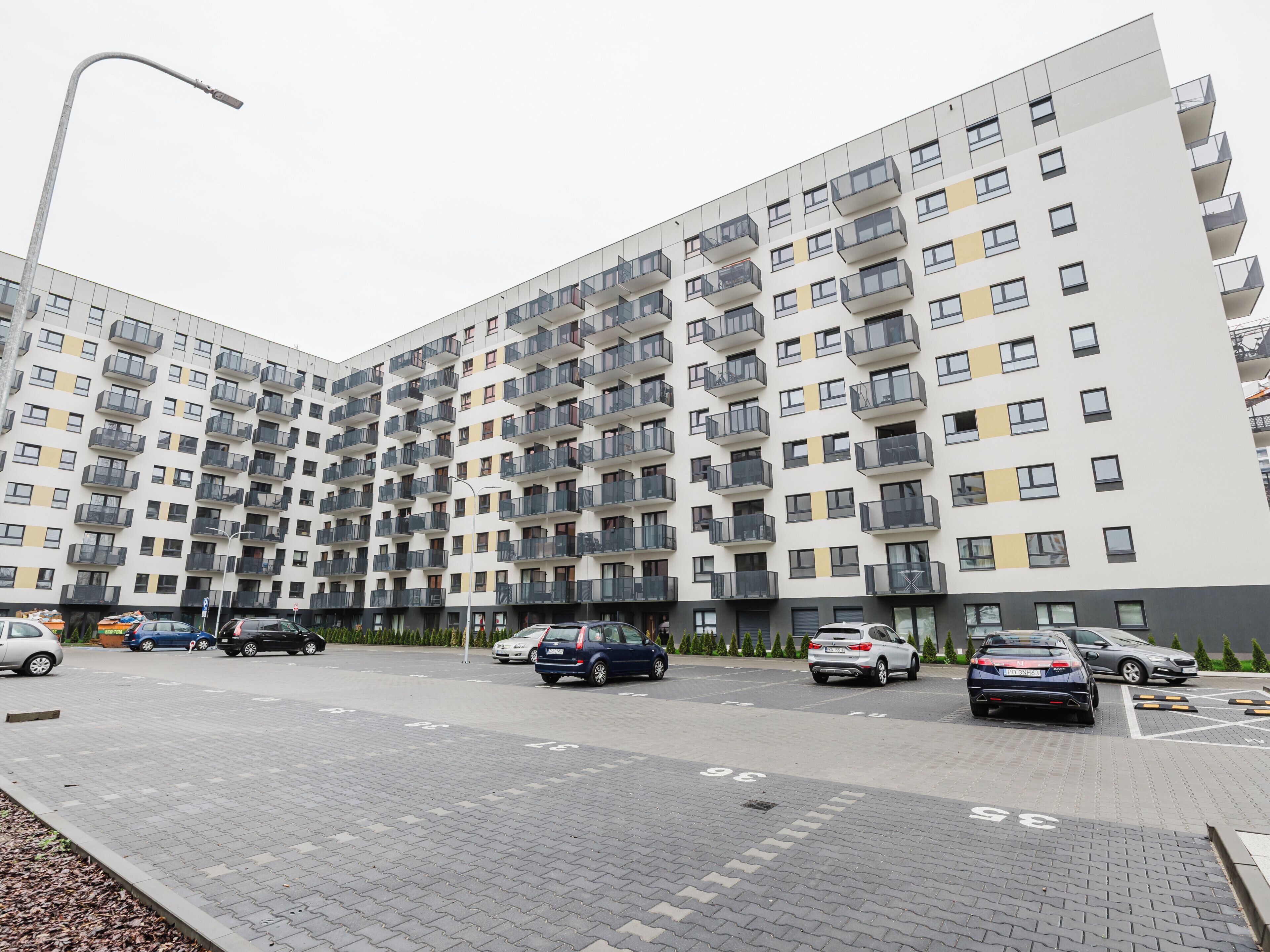 Un edificio residencial de varios pisos con balcones, una zona de estacionamiento y una farola.