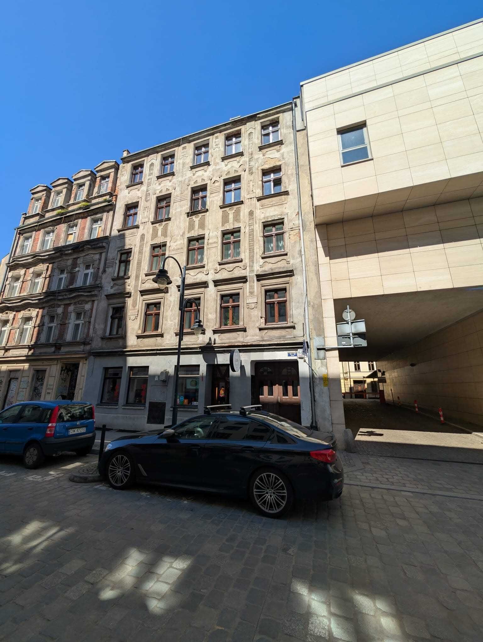 Um edifício de vários andares com estilo arquitetônico clássico, apresentando uma combinação de fachadas de tijolo e pedra, janelas grandes e uma entrada imponente com portão de metal.