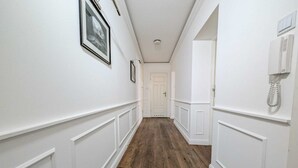 Un couloir aux murs blancs, doté d’un plancher en bois et d’une porte blanche au fond.