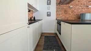 Une cuisine étroite avec des meubles blancs, un mur en briques et un plan de travail noir.