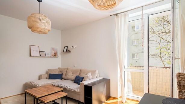 A modern living room with a sofa, a coffee table, and a black TV stand. There is a large window with a view of a building and trees. - Rondo Wiatraczna Stylish Apartment (Warszawa)