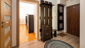 A room with a wooden floor, a dark wooden wardrobe, a small bench, and a patterned rug. - Rondo Wiatraczna Stylish Apartment (Warszawa)