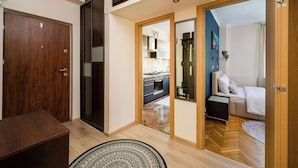 A modern interior with a wooden floor, a dining table, and a kitchen visible through an open door. - Rondo Wiatraczna Stylish Apartment (Warszawa)
