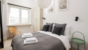A modern bedroom with a large bed, a window, a chair, and artwork on the wall.