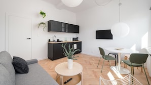 A modern living space with a grey sofa, a round wooden table, and a kitchen area with black cabinets and a white countertop.