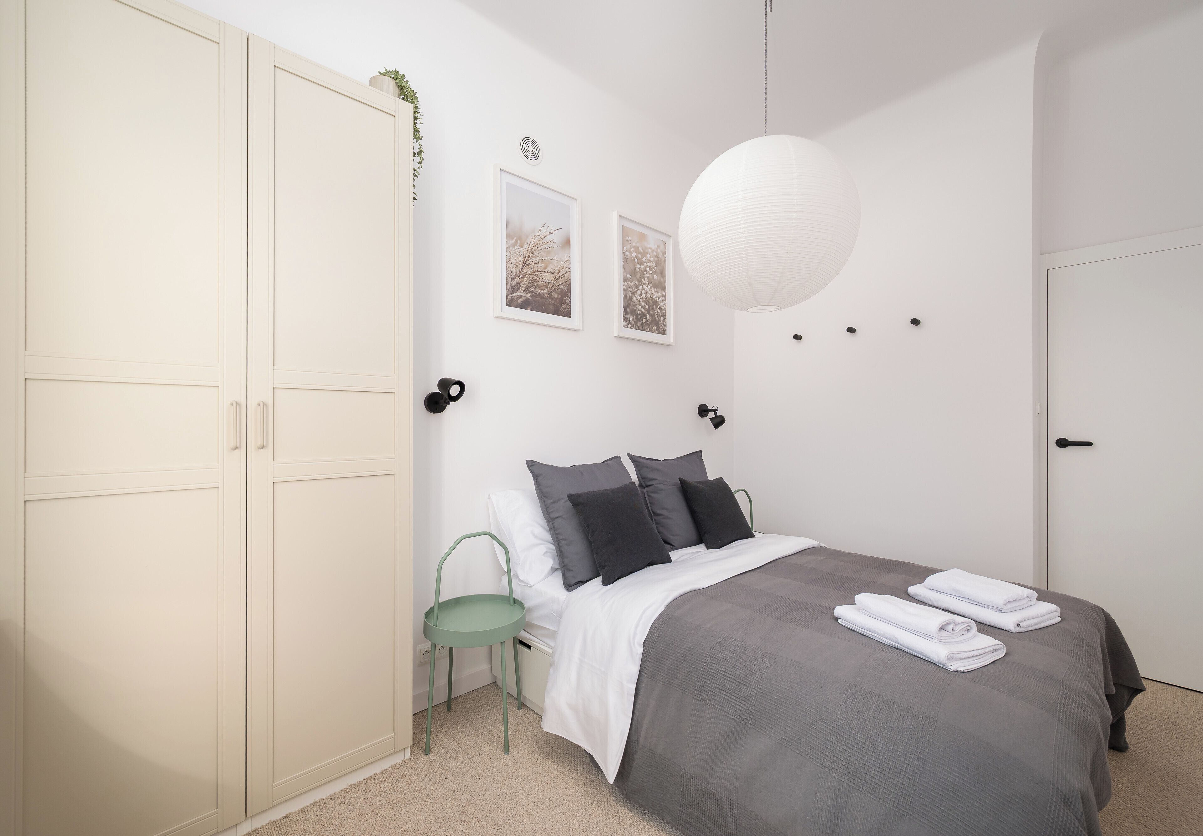 Un dormitorio con una cama, una silla verde, un armario blanco y dos cuadros en la pared.