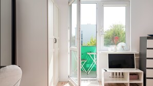 Ett modernt rum med en skjutdörr i glas som leder ut till en balkong, ett vitt TV-bord och ett litet bord med en stol.