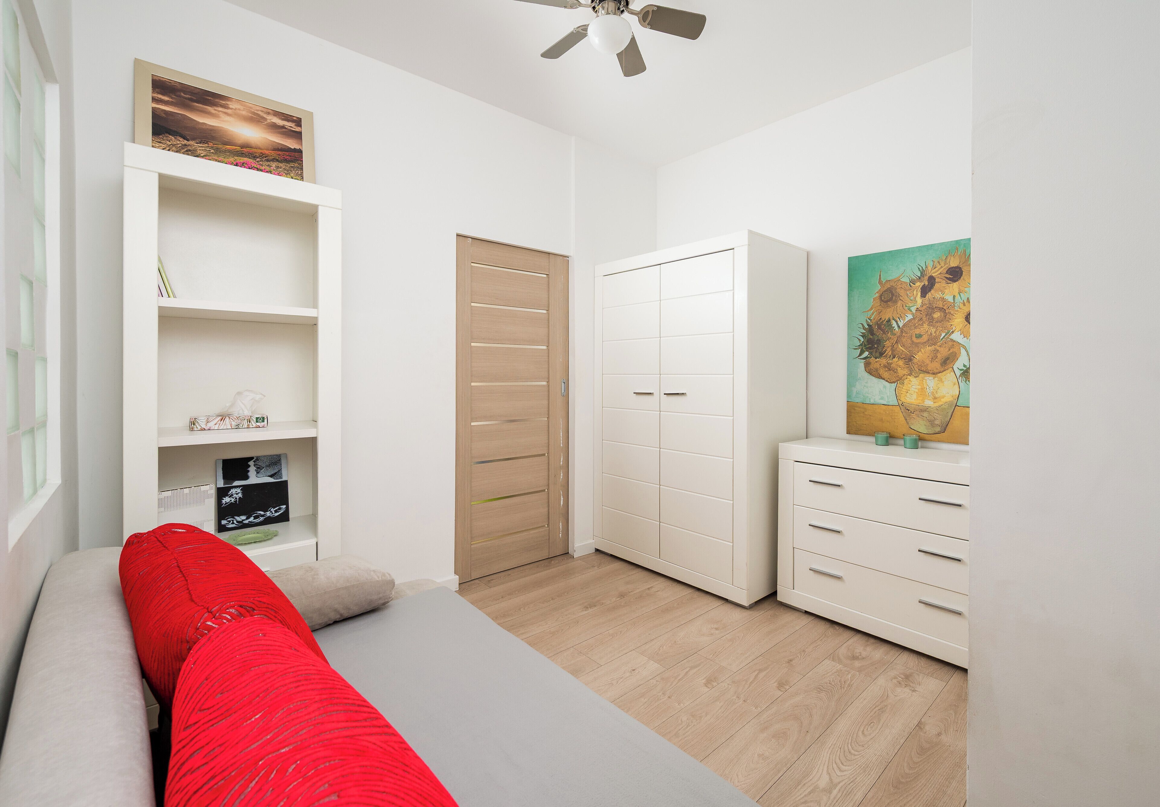 A bedroom with a bed, a wardrobe, a dresser, and a shelf with decorative items.
