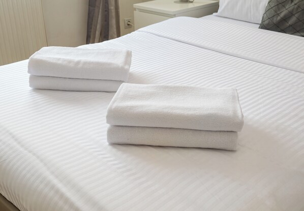 Una cama bien hecha con sábanas blancas y dos toallas dobladas a un lado.