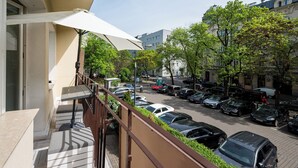 Un balcone con un ombrellone bianco, un parcheggio con diverse auto e edifici sullo sfondo.