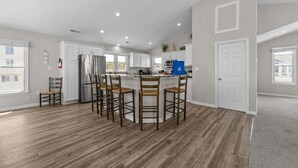 A modern kitchen with a central island, white cabinetry, and a wooden floor. - Dune Fabulous | 1,200 ft to the beach | Private Pool, Hot Tub, and Dog Friendly (Corolla)