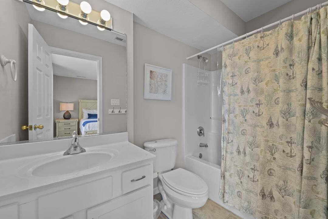 A bathroom with a vanity, sink, mirror, and a shower curtain with a marine pattern.