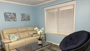 Ein Wohnzimmer mit einem beigefarbenen Sofa, einem dunklen Holztisch und einem Korbstuhl.