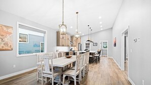 Une cuisine spacieuse avec des meubles en bois, un coin repas doté d’une grande table et de chaises, et un éclairage suspendu.