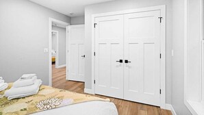 A hotel room with a bed, a set of white wardrobes, and a wooden floor.