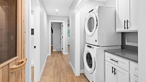 A laundry room with stacked washers and dryers, wooden flooring, and white cabinetry. - RiverWest Northwoods-Base -Hot Tub -Sauna -Dogs (Duluth)
