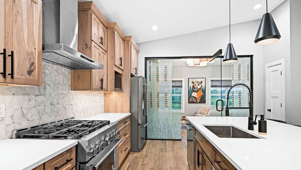 A modern kitchen with wooden cabinets, a stainless steel range hood, a gas stove, a refrigerator, and a large island with a sink. - RiverWest Northwoods-Base -Hot Tub -Sauna -Dogs (Duluth)