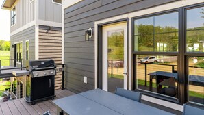 An outdoor patio with a grill, a table, and a sliding glass door leading to a parking area. - RiverWest Northwoods-Base -Hot Tub -Sauna -Dogs (Duluth)