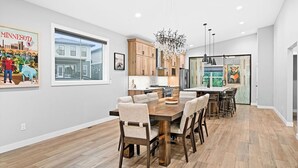 A modern kitchen with wooden cabinets, a large dining table, and a chandelier. - RiverWest Northwoods-Base -Hot Tub -Sauna -Dogs (Duluth)