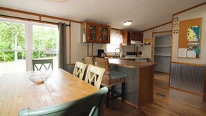 A kitchen with wooden cabinets, a dining table with chairs, a small island with a sink, and a view of greenery outside.