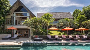 A poolside area with sun loungers and umbrellas, a modern house with a sloped roof, and lush greenery. - Luxe Vacay Atulya Residence | Chef & Staff | LTH-1 (Koh Sumui)