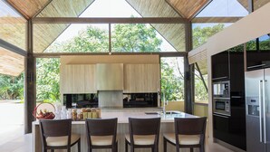 A modern kitchen with a large island, built-in appliances, and a view of greenery outside. - Luxe Vacay Atulya Residence | Chef & Staff | LTH-1 (Koh Sumui)