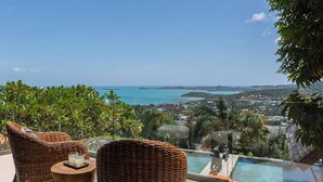 A balcony with wicker furniture, a glass table, and a view of a coastal landscape. - Luxe Vacay Atulya Residence | Chef & Staff | LTH-1 (Koh Sumui)