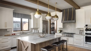 Una cocina moderna con armarios blancos, una isla grande con taburetes de bar, electrodomésticos de acero inoxidable y un salpicadero con diseño de espiga.