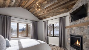 Un dormitorio con una cama grande, chimenea de piedra y vistas al exterior.